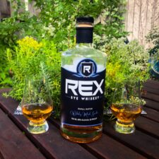 a photo of a whiskey bottle and two glasses against a greenery backdrop