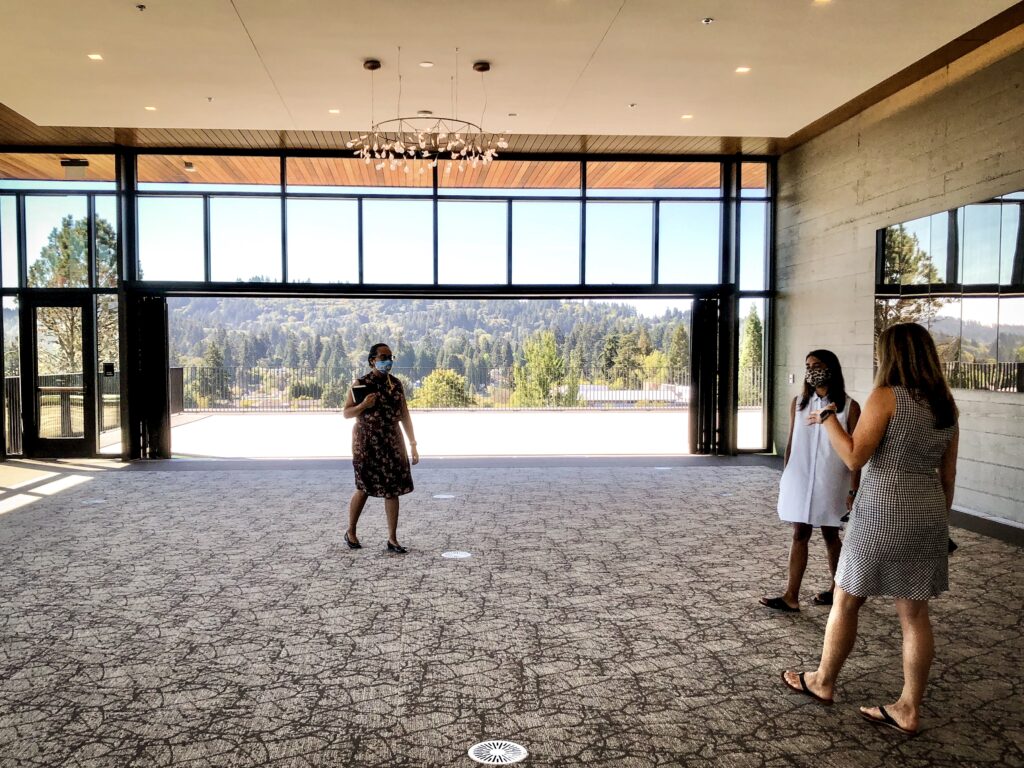 Portland event planning photo of 3 women standing in a ballroom under a chandelier. A view of Lake Oswego Oregon is behind them.